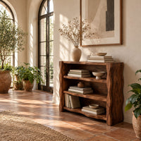 Open shelf console table with thick wavy edged side panels in a bright entryway with arched windows and plants