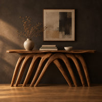 Wooden console table with a wavy top on a row of arched legs in a dark studio against a charcoal plaster wall