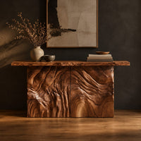 Console table on a block base carved with rippled ridges in a dark studio against a charcoal plaster wall