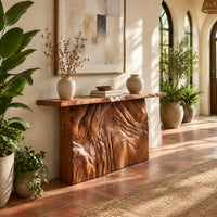 Console table on a block base carved with rippled ridges in a bright entryway with arched windows and plants