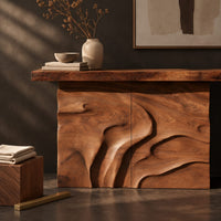 Corner detail of console table on a solid base carved with flowing relief beside wood, brass and linen samples