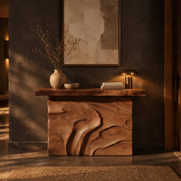 Console table on a solid base carved with flowing relief in a dark entryway at golden hour