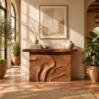 Console table on a solid base carved with flowing relief in a bright entryway with arched windows and plants
