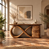 Console table with an infinity loop base and a stacked block at one end in a bright entryway with arched windows and plants