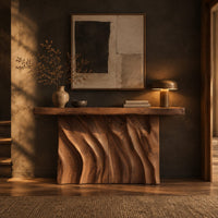 Console table with a thick slab top and a deeply carved two panel body in a dark entryway at golden hour