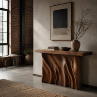 Console table with a thick slab top and a deeply carved two panel body in an industrial loft entryway with exposed brick