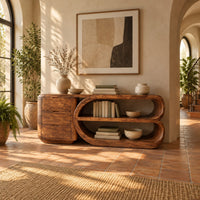 Console table with a three drawer block and a looped open shelf unit in a bright entryway with arched windows and plants