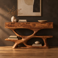 Console table with three drawers over a twisting open loop base and low shelf in a dark studio against a charcoal plaster wall