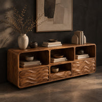 Low console cabinet with three open cubbies above two wave carved front panels, three-quarter view showing the grain