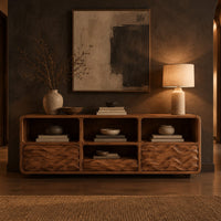 Low console cabinet with three open cubbies above two wave carved front panels in a dark entryway at golden hour