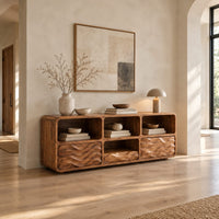 Low console cabinet with three open cubbies above two wave carved front panels in a bright open plan entryway