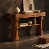 Corner detail of console table with two waisted sculpted legs and a single open shelf below beside wood, brass and linen samples