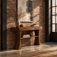 Console table with two waisted sculpted legs and a single open shelf below in an industrial loft entryway with exposed brick