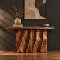 Console table with a wave carved fluted base and a live edge top in a dark studio against a charcoal plaster wall