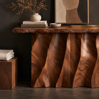 Corner detail of console table with a wave carved fluted base and a live edge top beside wood, brass and linen samples
