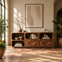 Console table with wave carved front panels and open cubbies in a bright entryway with arched windows and plants