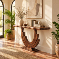 Wood console table with a wavy edge top on a layered arc base in a bright entryway with arched windows and plants