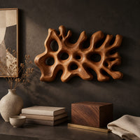 Corner detail of wide wall sconce shaped like branching coral with pierced openings beside wood, brass and linen samples