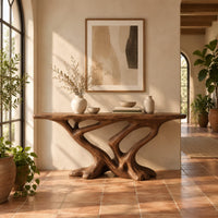 Console table with a slab top on crossing limbs and root style feet in a bright entryway with arched windows and plants