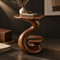 Corner detail of curling swirl side table with a wide top and a small nested disc shelf beside wood, brass and linen samples