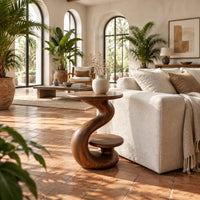 Curling swirl side table with a wide top and a small nested disc shelf in a bright living room with arched windows and plants