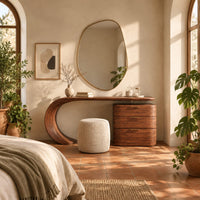 Makeup vanity with a sweeping curved leg and a block of three drawers in a bright bedroom with arched windows and plants