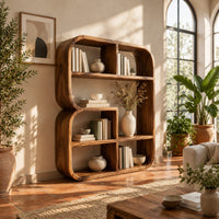 Bookshelf with a thick curved frame and open cubbies of mixed sizes in a bright living room with arched windows and plants