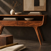 Corner detail of curved console table with two drawers, open shelf and tapered legs beside wood, brass and linen samples