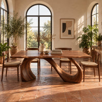 Dining table with a slim top on a looping curved ribbon base in a bright dining room with arched windows and plants