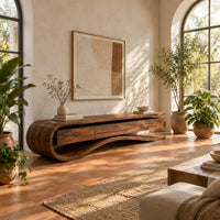 Low tv stand with a curled end and a wavy ribbon base in a bright living room with arched windows and plants
