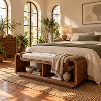 Curved bench with a tufted seat cushion and two open cubbies below in a bright bedroom with arched windows and plants
