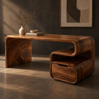 Corner detail of waterfall desk with a curved top and a scroll shaped drawer pedestal beside wood, brass and linen samples