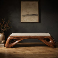 Cushioned bench with a sculpted wood arch base and oval cutouts in a dark studio against a charcoal plaster wall