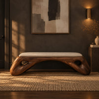 Cushioned bench with a sculpted wood arch base and oval cutouts in a dark entryway at golden hour