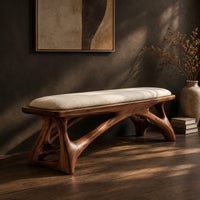Padded bench with a pale seat on sculpted branching wood legs, three-quarter view showing the grain