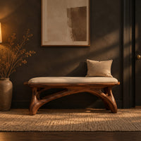 Padded bench with a pale seat on sculpted branching wood legs in a dark entryway at golden hour