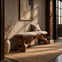 Padded bench with a pale seat on sculpted branching wood legs in an industrial loft entryway with exposed brick