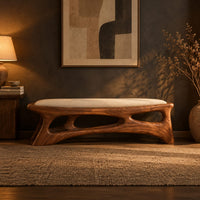 Cushioned bench with a carved open frame and slanted legs in a dark entryway at golden hour