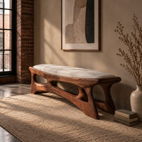 Cushioned bench with a carved open frame and slanted legs in an industrial loft entryway with exposed brick