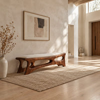 Cushioned bench with a carved open frame and slanted legs in a bright open plan entryway