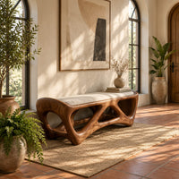 Cushioned bench with an open lattice wood base in a bright entryway with arched windows and plants