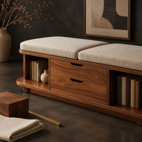 Corner detail of low bench with two seat cushions, two center drawers and open end shelves beside wood, brass and linen samples