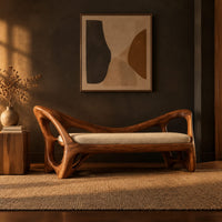 Bench with a cream seat cushion and a sculpted frame full of open cutouts in a dark entryway at golden hour