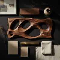 Detail of wooden slab wall art with carved oval openings beside wood, brass and linen samples