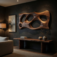 Wooden slab wall art with carved oval openings above a low console in an evening living room