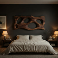 Wooden slab wall art with carved oval openings above a bed in a dusk lit bedroom