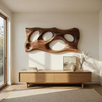 Wooden slab wall art with carved oval openings above a light oak sideboard in daylight