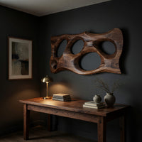Wooden slab wall art with carved oval openings above a desk in a dark study corner