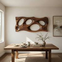 Wooden slab wall art with carved oval openings beside a dining table in natural light