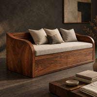 Corner detail of daybed style sofa with swept wood sides, paneled base and a long seat pad beside wood, brass and linen samples
